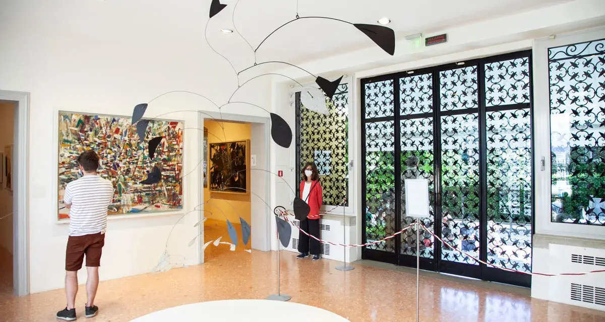 Un uomo ammira un quadro astratto, mentre una donna osserva una scultura mobile. Un'atmosfera d'arte al Peggy Guggenheim di Venezia.