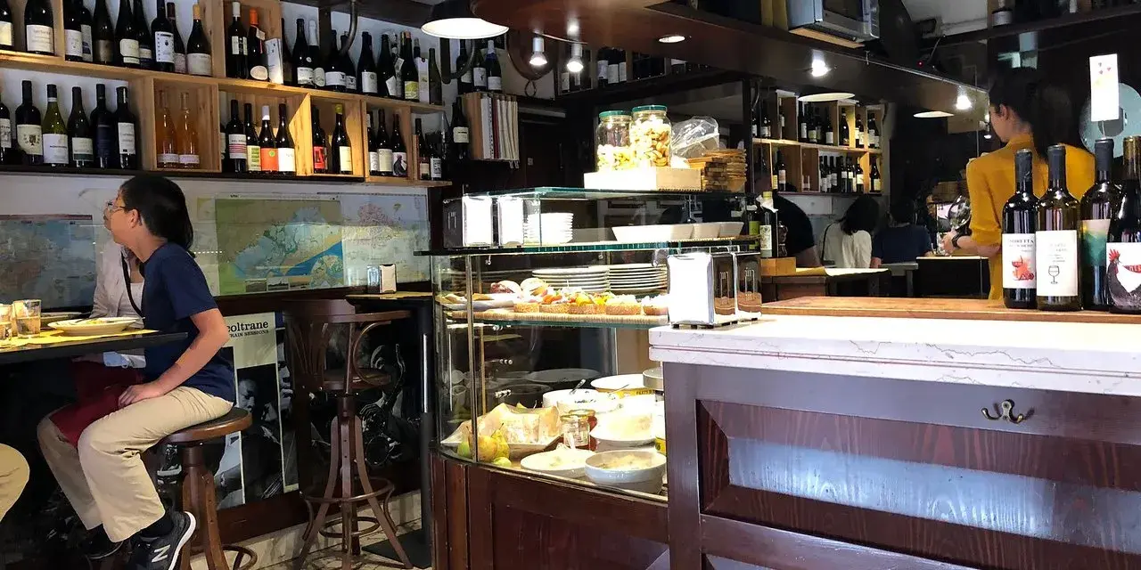 Interno di un'osteria al cicheto a Venezia, con bottiglie di vino, cibi in vetrina e persone sedute al bancone.