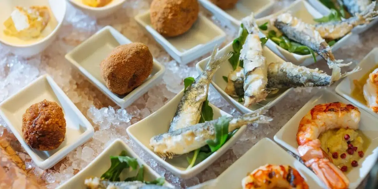 Assaggio di prodotti tipici veneziani: crocchette dorate, sarde fritte e gamberi grigliati, presentati su un letto di ghiaccio.
