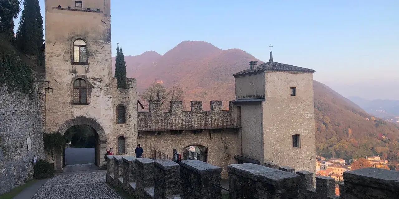Antico borgo di Cison di Valmarino con torri e mura di pietra, sullo sfondo colline autunnali.