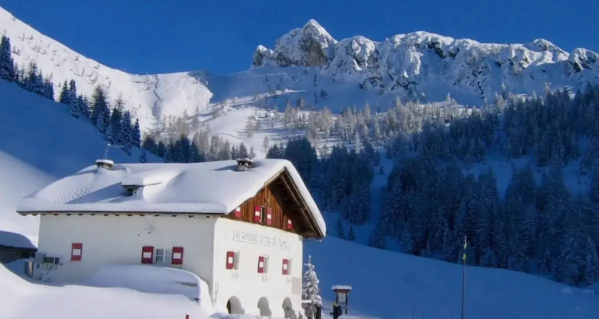Rifugio innevato nelle Dolomiti, ideale per ciaspolate invernali. Montagne maestose e boschi coperti di neve.