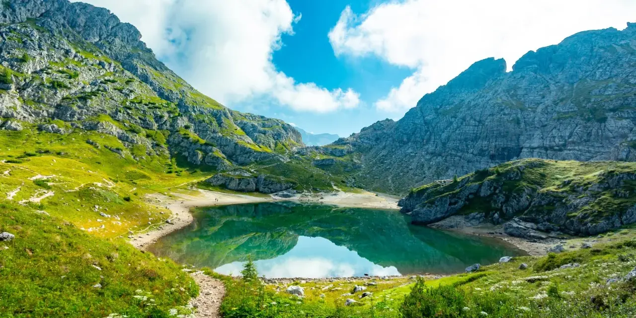 Sentiero panoramico verso un lago alpino turchese, incorniciato da montagne maestose. Un vero gioiello dell'alta via Dolomiti più bella.