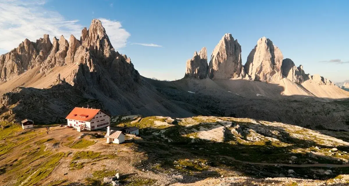 Rifugio con tetto rosso e montagne imponenti, un'oasi di pace tra i rifugi Dolomiti Bellunesi facili, ideale per un'escursione panoramica.