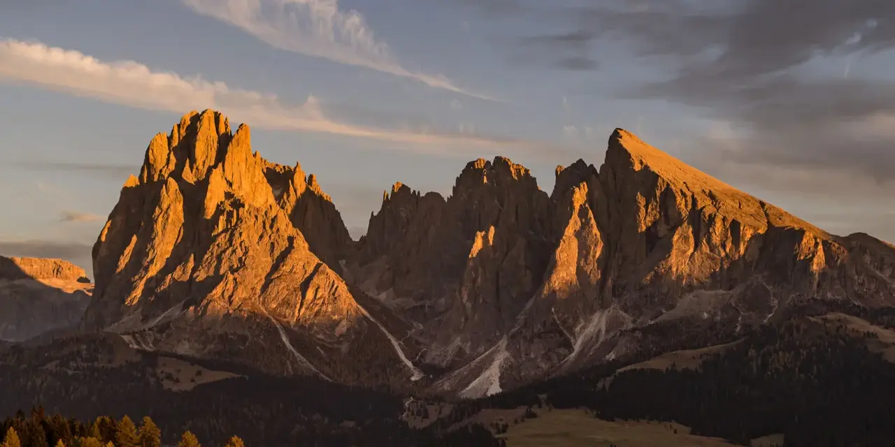 Le maestose **Dolomiti Rosse** illuminate dal sole al tramonto, con cime aguzze e pendii boscosi.