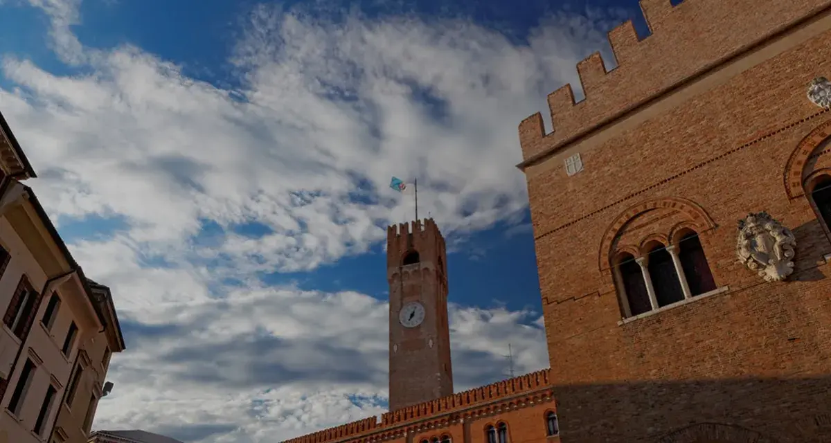 Torre dell'Orologio e palazzi storici a Treviso, un viaggio da Padova a Treviso sotto un cielo azzurro e nuvoloso.