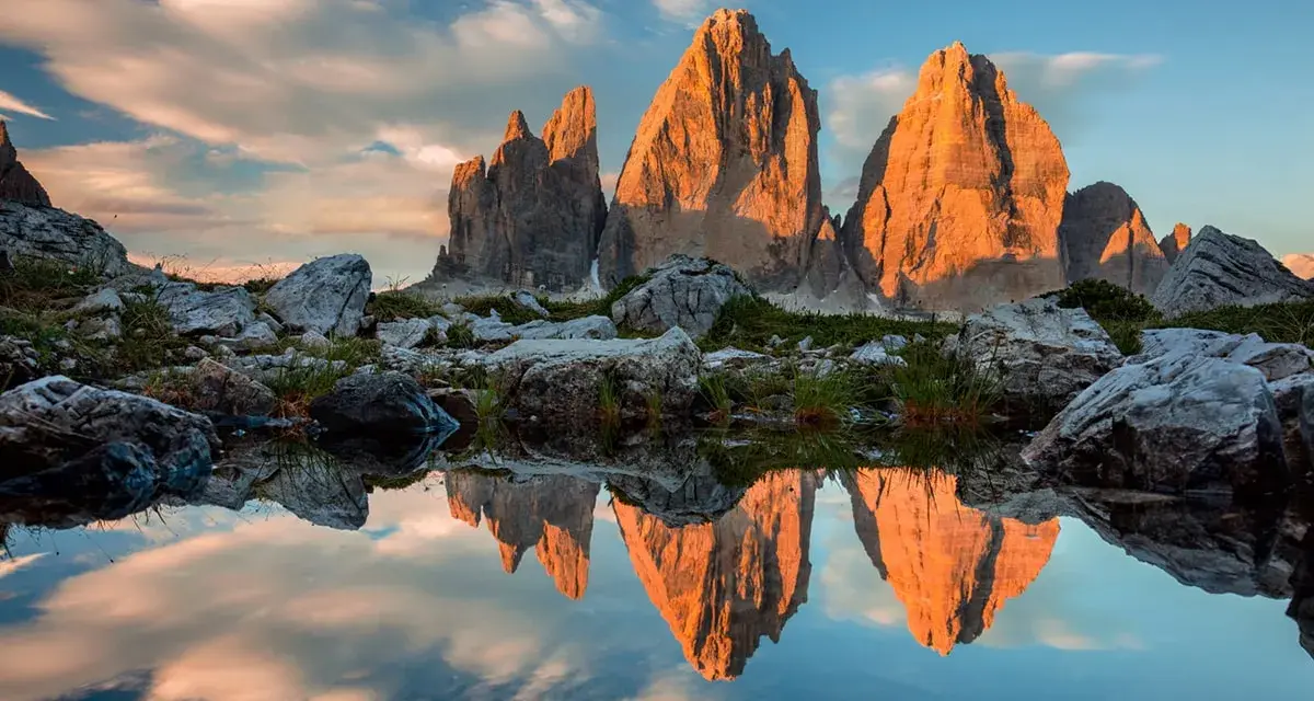 Le Tre Cime di Lavaredo illuminate dal tramonto, riflesse in uno specchio d'acqua. Un paesaggio che incarna la bellezza dei **Dolomiti paesi più belli**.