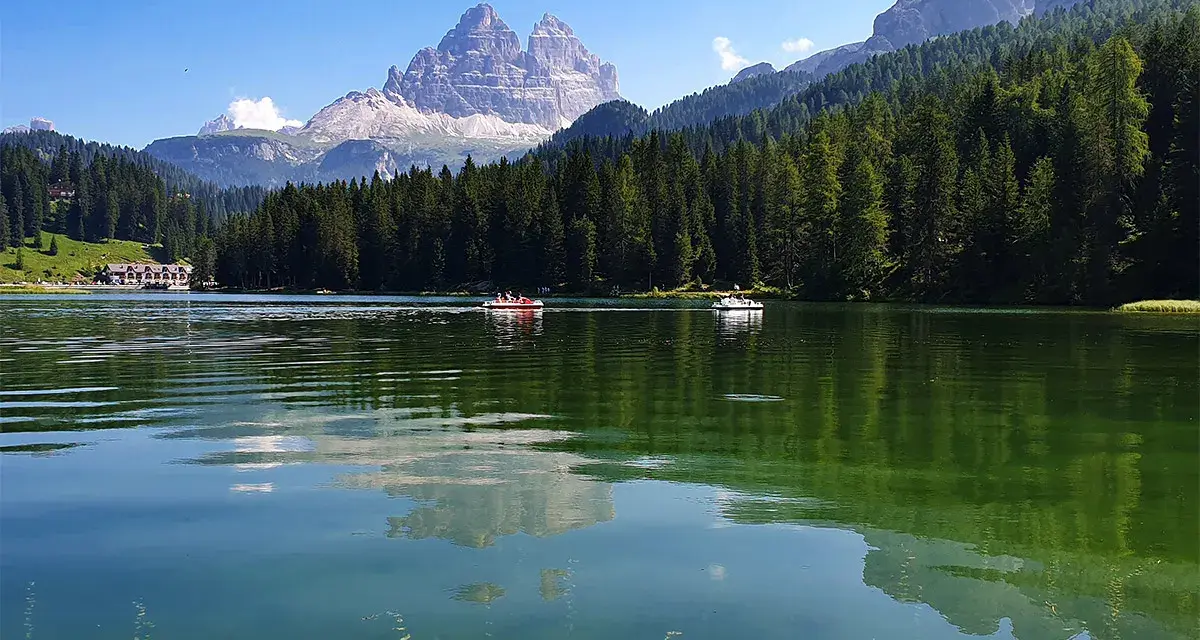 Il **lago di Misurina** incanta con le sue acque verdi e le montagne maestose. Barchette a remi solcano la superficie, riflettendo il cielo azzurro e la foresta di abeti.