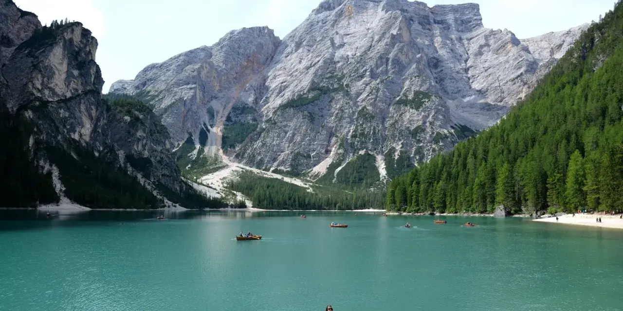 Lago turchese con barche a remi e maestose montagne veneto sullo sfondo.