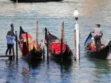 Gondole veneziane ornate, una turista scatta foto. La differenza tra gondola e sandalo è chiara: una naviga, l'altro si indossa.