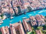 Vista aerea del **canale di Venezia** con gondole e vaporetti che navigano tra palazzi storici dai tetti rossi.
