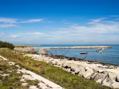 Sentiero in pietra e mare calmo con barche. Per capire come arrivare a Pellestrina da Fusina, immagina di percorrere questa costa.