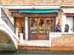 Coppia davanti a una delle tipiche osterie a Venezia, con bottiglie di vino in esposizione.