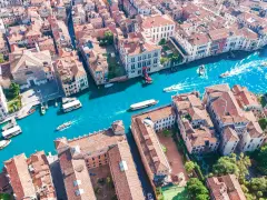 Vista aerea del **canale di Venezia** con gondole e vaporetti che navigano tra palazzi storici dai tetti rossi.