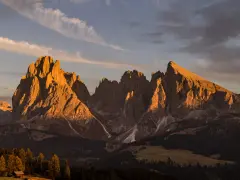 Le maestose **Dolomiti Rosse** illuminate dal sole al tramonto, con cime aguzze e pendii boscosi.