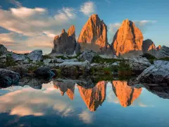 Le Tre Cime di Lavaredo illuminate dal tramonto, riflesse in uno specchio d'acqua. Un paesaggio che incarna la bellezza dei **Dolomiti paesi più belli**.