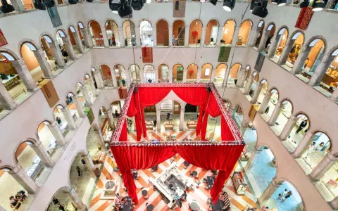 Interni del Fondaco dei Tedeschi con un'installazione di tende rosse al centro, che incornicia un'area bar e tavoli. Le arcate dei piani superiori ospitano negozi.