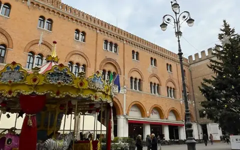 Carosello colorato e albero di Natale in piazza, scorci di cosa vedere a Treviso con palazzi storici e gente che passeggia.