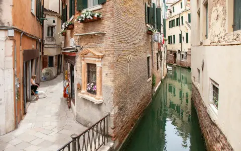 Un vicolo stretto e un canale a Venezia, con una donna e un cane seduti, tra i tanti **Venezia posti da visitare**.