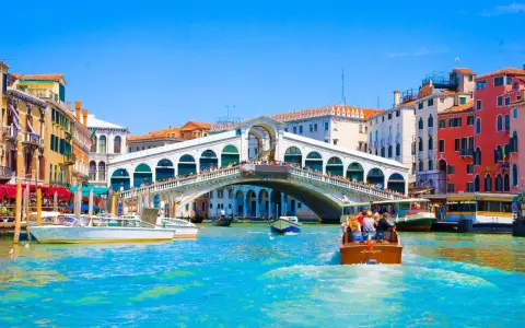 Gondole e vaporetti solcano il Canal Grande, sotto il Ponte di Rialto affollato di gente. Un assaggio delle **esperienze Venezia**.