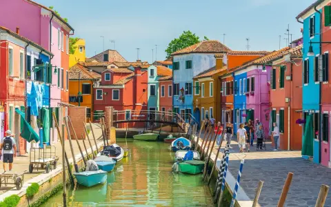 Colorate case affacciate su un canale a Venezia, con barche ormeggiate e persone che passeggiano. Le fondamenta sono un tripudio di colori vivaci.