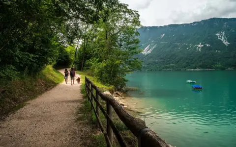 Coppia con cane passeggia lungo il sentiero del lago di Santa Croce, godendosi la natura e il panorama montano.