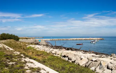 Sentiero in pietra e mare calmo con barche. Per capire come arrivare a Pellestrina da Fusina, immagina di percorrere questa costa.