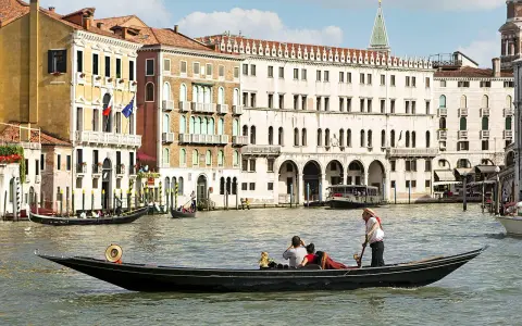 Gondola con turisti e gondoliere, sullo sfondo palazzi storici e altre barche tipiche veneziane.