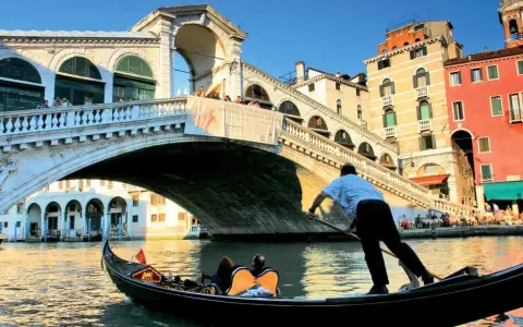 Gondola sotto il Ponte di Rialto, un'icona delle piazze Venezia, con edifici colorati e turisti che ammirano il panorama.