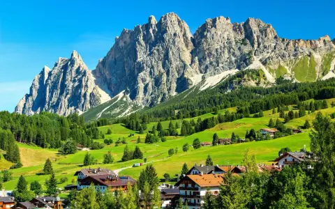 Un viaggio da Venezia a Cortina: verdi pascoli, boschi rigogliosi e imponenti vette dolomitiche incorniciano un villaggio alpino.
