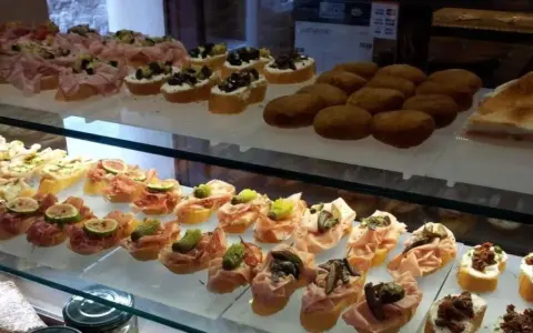 Vetrina piena di **migliori cicchetti Venezia**: crostini con affettati, fichi, olive e verdure. Un tripudio di sapori da gustare.