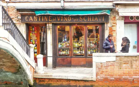 Coppia davanti a una delle tipiche osterie a Venezia, con bottiglie di vino in esposizione.