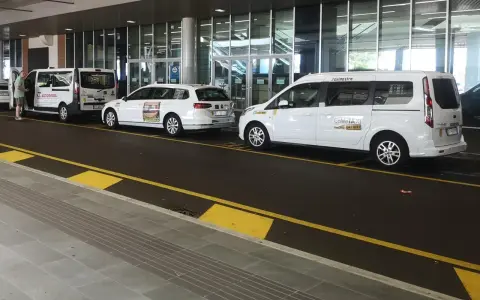 Taxi a Venezia, in attesa all'aeroporto. Diverse auto bianche, tra cui minivan e station wagon, pronte per il trasporto passeggeri.