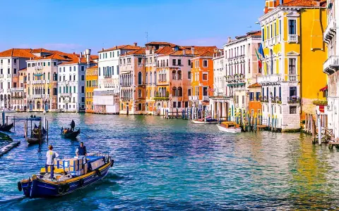Venezia: turisti in gondola e vaporetti sul Canal Grande, tra palazzi colorati e acque azzurre.