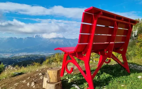 La panchina gigante sul Nevegal, rossa e imponente, domina un panorama mozzafiato di montagne e vallate sotto un cielo azzurro.