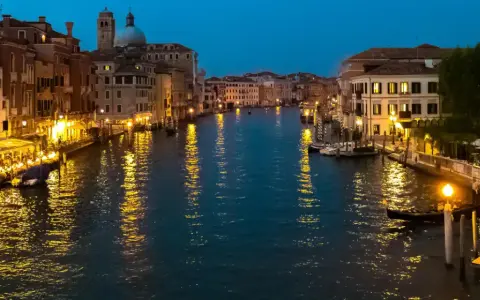 Serata magica per visitar Venezia: luci dorate sui palazzi e riflessi sull'acqua del Canal Grande, con gondole e ristoranti animati.