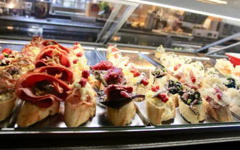 Assortimento di cicchetti in una vetrina di un'osteria veneziana: crostini con salumi, pesce e verdure.