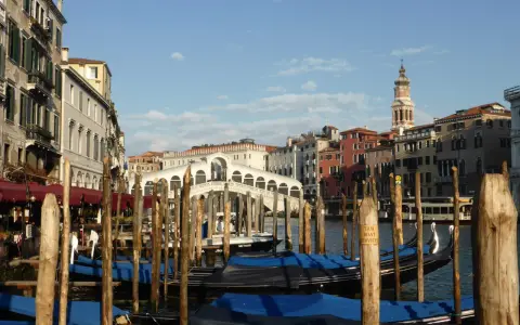 Gondole ormeggiate nel Canal Grande, con il Ponte di Rialto sullo sfondo. Un'immagine di Venezia romantica, con palazzi storici e il cielo azzurro.