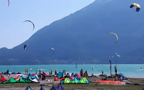 Coloratissima spiaggia sul lago di Santa Croce, con kitesurfisti che sfrecciano sull'acqua turchese e vele colorate che ondeggiano al vento.
