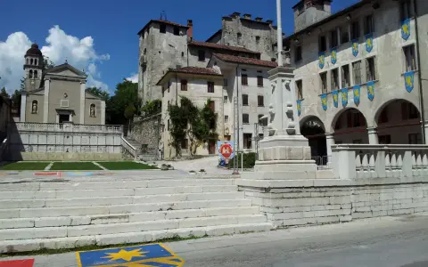 Piazza con scalinata, chiesa e castello: ecco cosa vedere a Feltre. Stendardi gialli decorano gli edifici storici.
