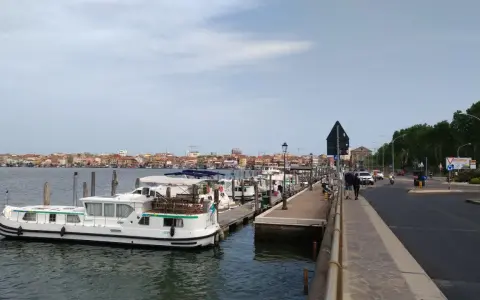 Un vaporetto attracca a Chioggia, con la città sullo sfondo e una strada trafficata.