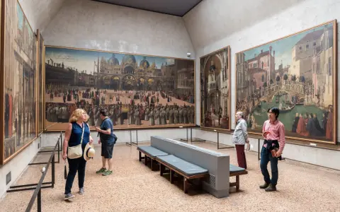 Visitanti ammirano grandi dipinti storici in uno dei musei d'arte a Venezia.