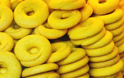 Una pila di dolcetti veneziani gialli, a forma di ciambella, con una texture leggermente ruvida.