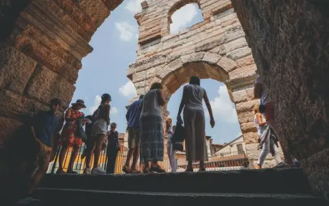 Turisti esplorano l'Arena di Verona, un'antica struttura che ricorda il Colosseo, sotto un cielo azzurro.