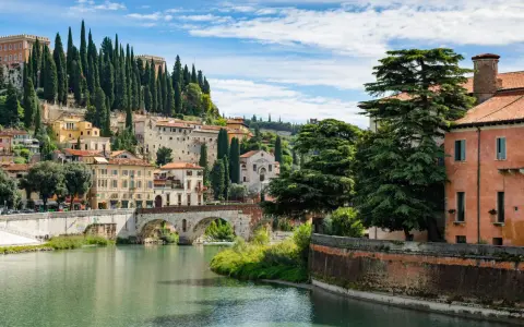 Un fiume attraversa Verona, con ponti storici e case colorate che salgono sulla collina. Un luogo incantevole da scoprire, tra le cose da vedere a Verona.