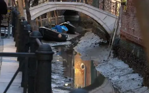 Canali di Venezia quasi asciutti, con barche arenate e riflessi di palazzi. Si vede quanto sono profondi i canali di Venezia in questa situazione insolita.