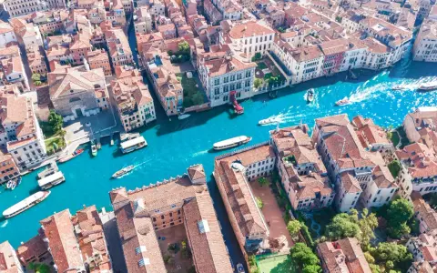 Vista aerea del **canale di Venezia** con gondole e vaporetti che navigano tra palazzi storici dai tetti rossi.