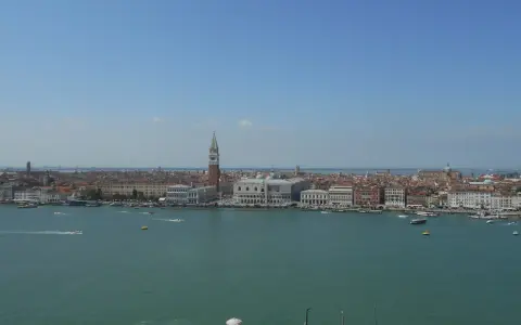 Venezia dall'alto, con il Campanile di San Marco che svetta tra i tetti rossi e il Canal Grande animato da vaporetti e barche.