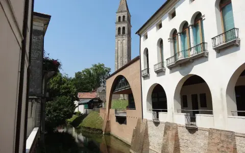 Canale e campanile a Oderzo, cosa vedere: un'elegante facciata bianca con portici e balconi si affaccia sull'acqua, con un ponte ad arco in mattoni.