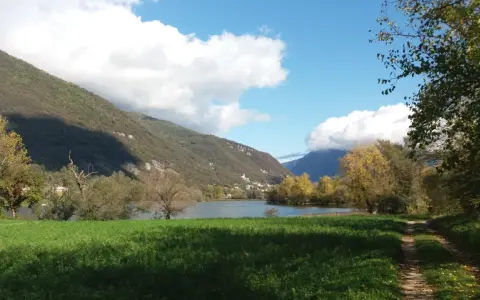 Sentiero per passeggiate in montagna Veneto, con lago, colline verdi e cielo azzurro con nuvole bianche.