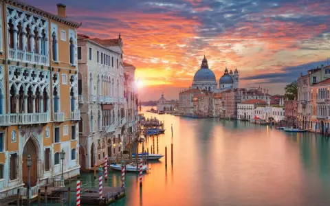 Tramonto sul Canal Grande, un quadro perfetto di posti romantici a Venezia. Palazzi storici e la Basilica di Santa Maria della Salute riflettono i colori del cielo.